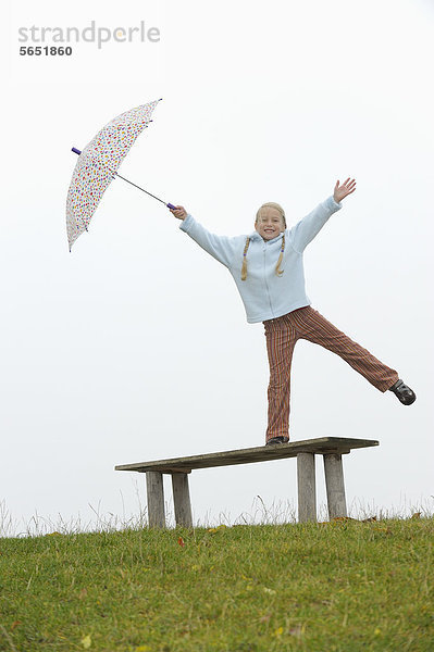 Mädchen steht auf Bank und hält Regenschirm  lächelt