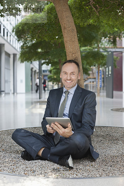 Deutschland  Leipzig  Geschäftsmann am Baum sitzend mit digitalem Tablett
