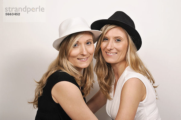 Zwillingsschwestern tragen Hüte in zu ihrer Kleidung entgegengesetzten Farben in Schwarz und Weiß