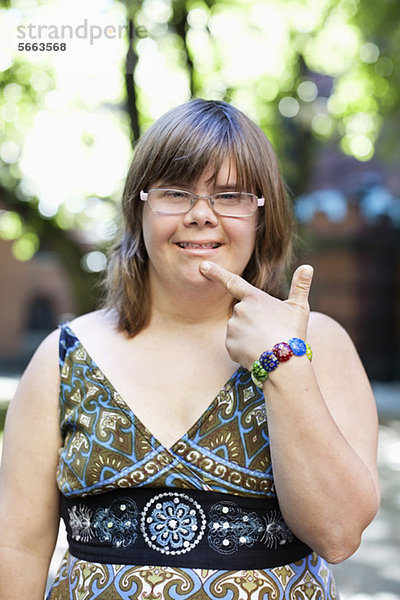 Porträt einer Frau mit Down-Syndrom  die mit dem Finger am Kinn lächelt  in Gebärdensprache.