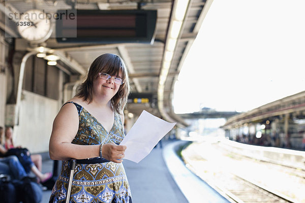 Lächelnde Frau mit Down-Syndrom wartet auf dem Bahnsteig mit Ticket