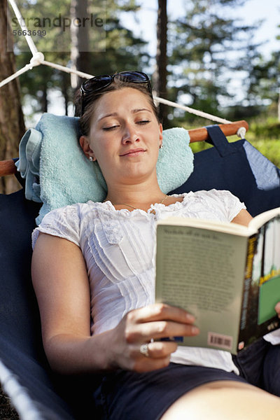 Junge Frau liest Buch über Hängematte