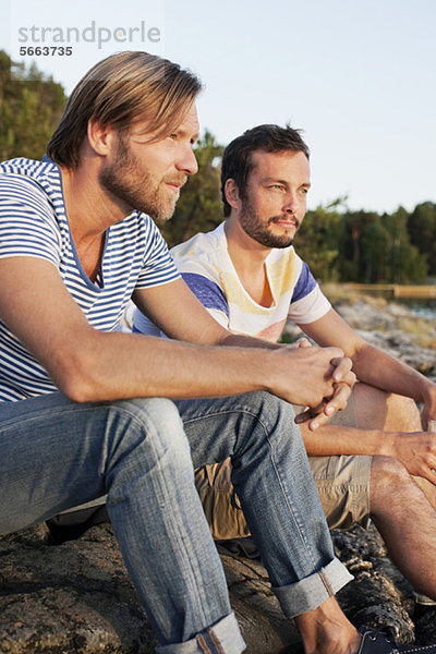 Zwei männliche Freunde  die auf dem Felsen sitzen und nachdenken.
