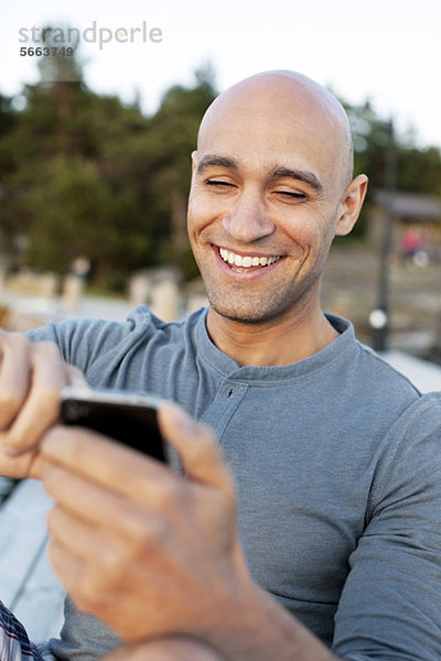 Mann lächelt  während Textnachrichten auf dem Handy gesendet werden