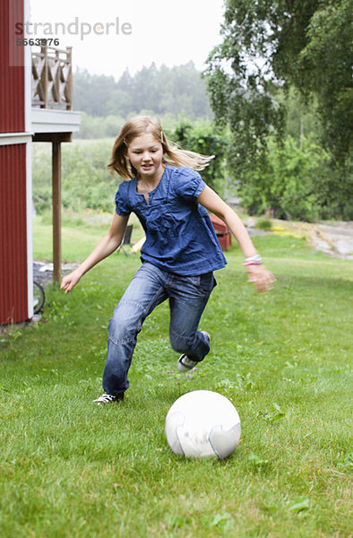 Vorpubertäres Mädchen spielt Fußball im Hinterhof