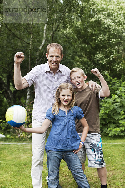 Porträt von aufgeregtem Vater und Kindern mit Fußball im Hinterhof