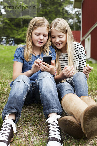 Schwestern sitzen im Hinterhof und schauen sich etwas im Handy an.