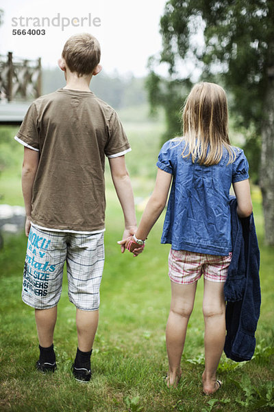 Rückansicht von Bruder und Schwester beim Händchenhalten