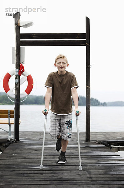 Portrait eines Jungen mit Krücken im Stehen auf einem Bein