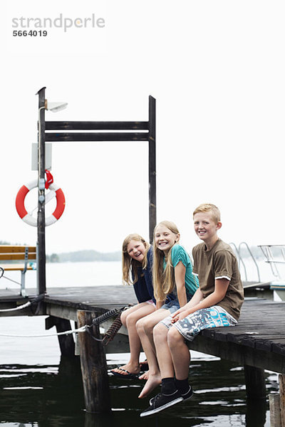 Geschwister sitzen Seite an Seite auf dem Pier