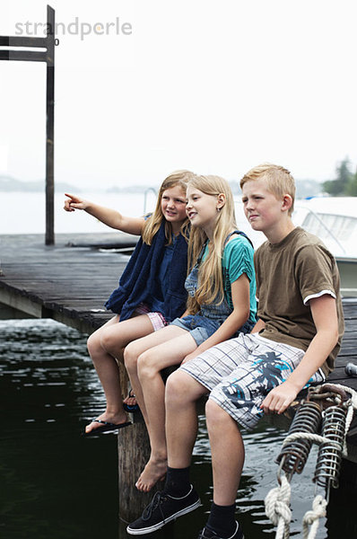 Bruder und Schwester sitzen Seite an Seite auf dem Pier