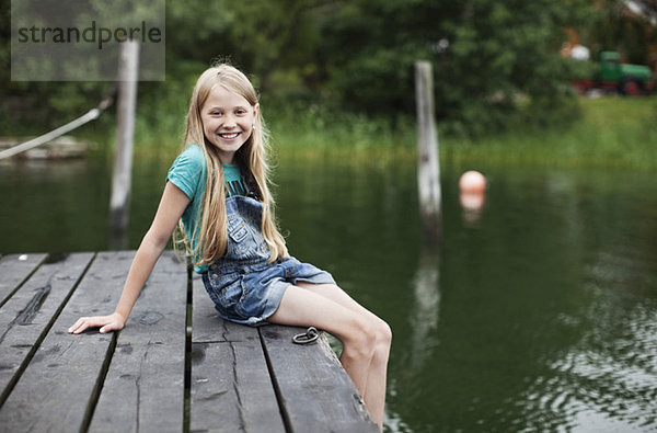 Porträt eines lächelnden blonden Mädchens am Pier im See