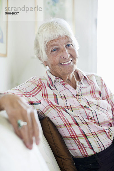 Porträt einer lächelnden Seniorin  die auf dem Sofa sitzt.