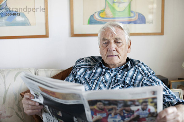 Senior erwachsener Mann beim Zeitungslesen im Wohnzimmer