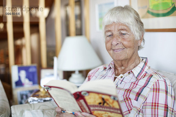 Glückliche Seniorin beim Lesen von Romanen im Liebeszimmer