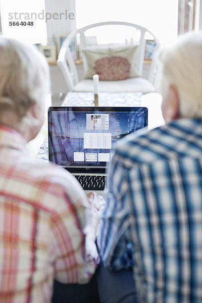 Aktives Seniorenpaar mit Laptop zusammen im Wohnzimmer