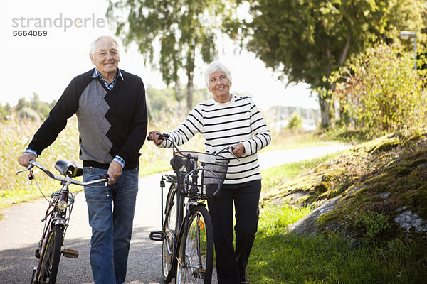 Seniorenpaar zu Fuß mit Fahrrädern im Park
