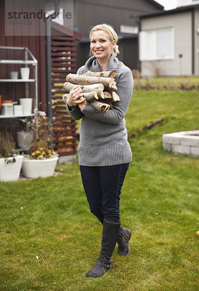 Porträt einer glücklichen mittleren erwachsenen Frau mit Brennholz im Hinterhof