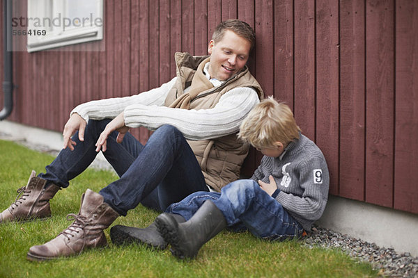 Vater und Sohn sitzen auf Gras im Garten.