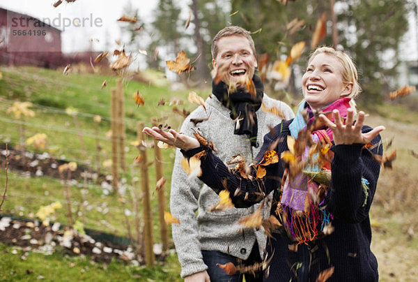 Paar genießt mit Herbstblättern  die auf sie fallen.