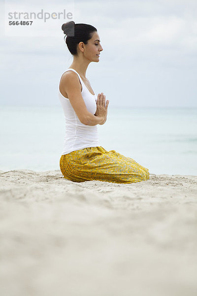 Reife Frau kniend in Gebetshaltung am Strand  Seitenansicht