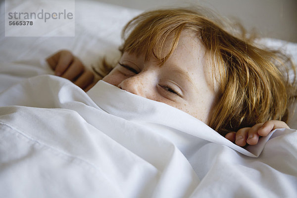 Junge im Bett liegend mit Bettlakenbezug Gesicht