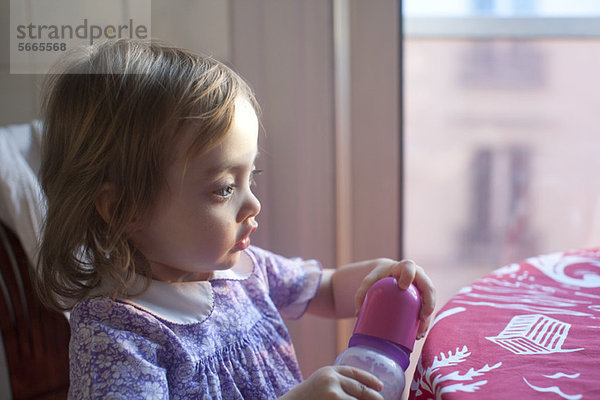 Kleinkind Mädchen hält Babyflasche  schaut in Gedanken weg