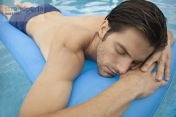 Junger Mann auf dem Bauch liegend auf einem aufblasbaren Schwimmer