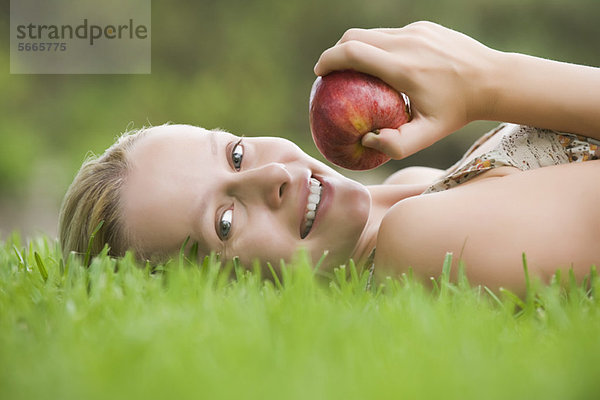 Junge Frau auf Gras liegend  Apfel haltend