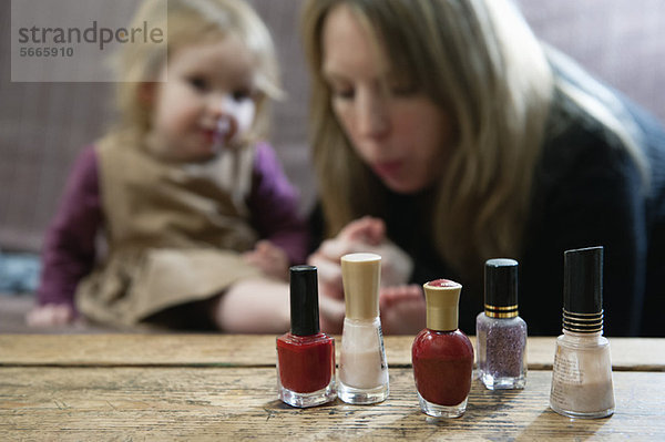 Flaschen mit Nagellack  die Mutter bläst auf die Zehen der kleinen Tochter im Hintergrund.