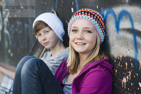 Teenagerin und Junge sitzen an einer Graffitiwand