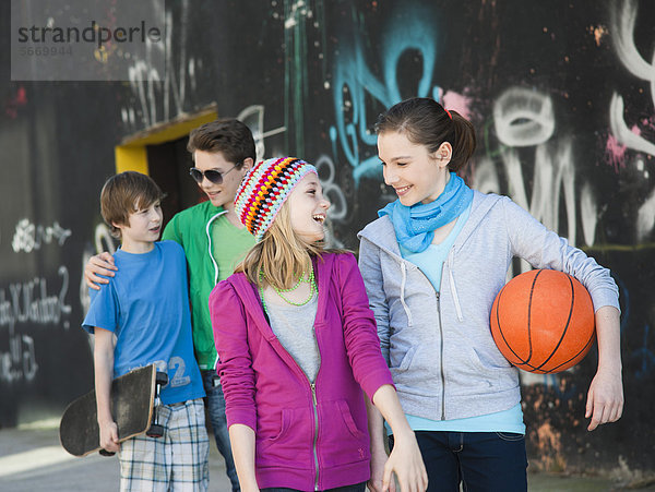 Vier fröhliche Teenager-Freunde gehen an einer Graffitiwand