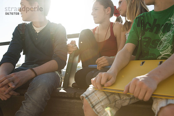 Vier Teenager-Freunde sitzen mit Mappen im Freien