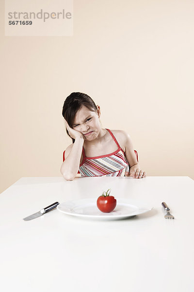 Schmollendes Mädchen sitzt am Tisch mit einer Tomate
