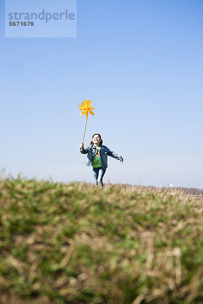 Mädchen rennt mit Windrädchen auf einer Wiese