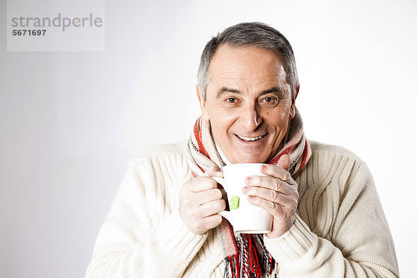 Fröhlicher Senior in Winterkleidung trinkt eine Tasse Tee