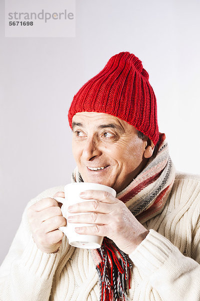 Fröhlicher Senior in Winterkleidung trinkt eine Tasse Tee