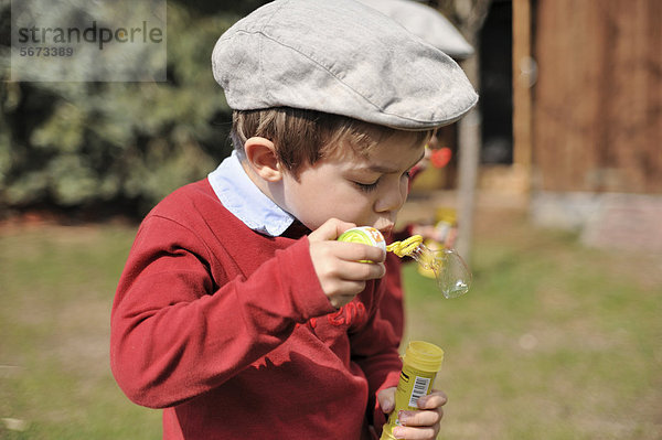 Junge  4 Jahre  mit Schiebermütze  macht Seifenblasen
