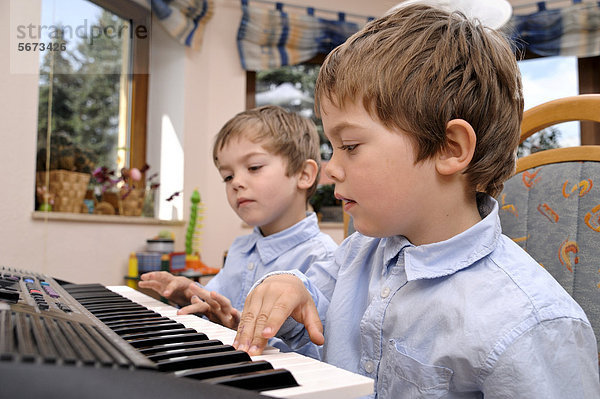 Zwillinge  Jungen  4 Jahre  machen gemeinsam Musik auf einem Keyboard