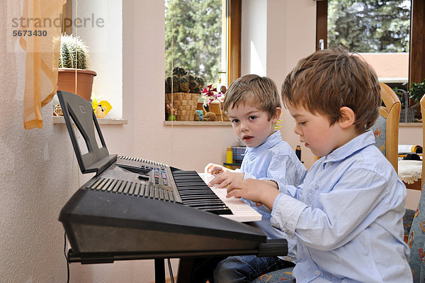 Zwei Zwillinge  Jungen  4 Jahre  machen gemeinsam Musik auf einem Keyboard