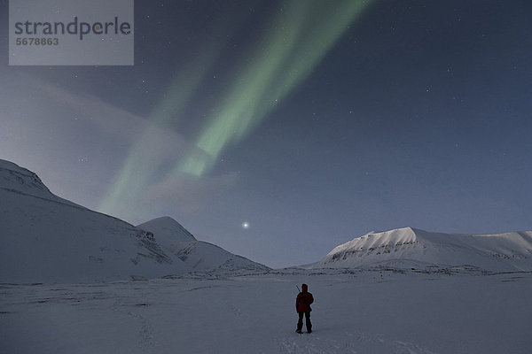 Person mit geschultertem Gewehr bestaunt Nordlichter und Sternenhimmel  Spitzbergen  Svalbard  Norwegen  Europa