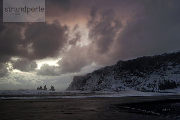 Stürmische Sonnenuntergangsstimmung am Strand bei VÌk  hinten die Felsnadeln Reynisdrangar  Südisland  Island  Europa
