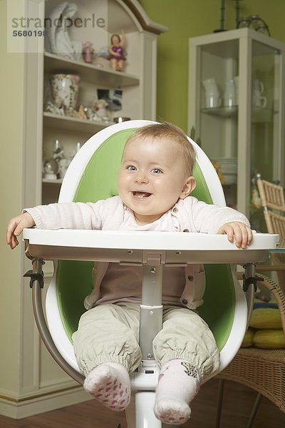 Fröhliches weibliches Baby sitzt im Hochstuhl