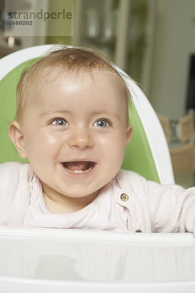 Fröhliches weibliches Baby sitzt im Hochstuhl