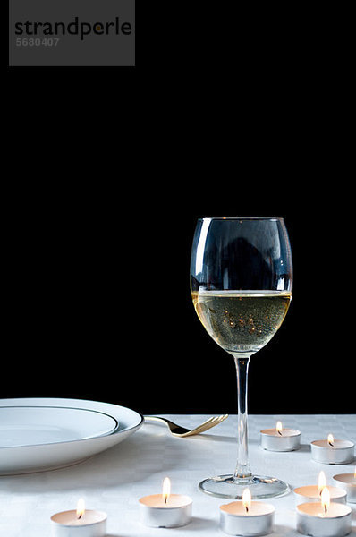 Glas Weißwein und Teelichter auf dem Tisch
