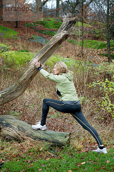 Reife Frau  die sich im Wald gegen einen Baum streckt.