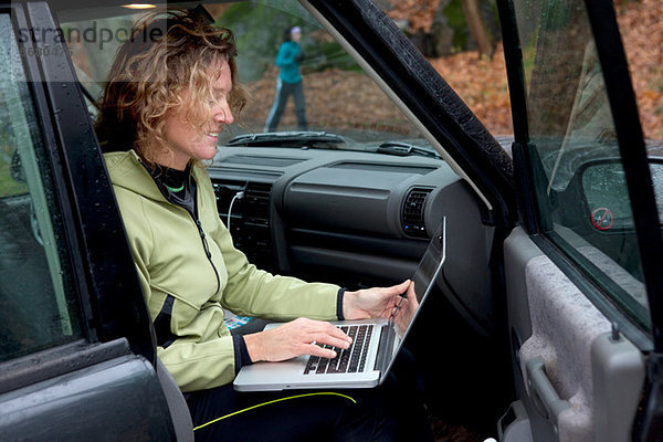 Reife Frau mit Laptop im Auto