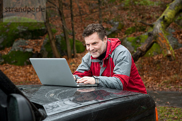 Erwachsener Mann mit Laptop an der Motorhaube