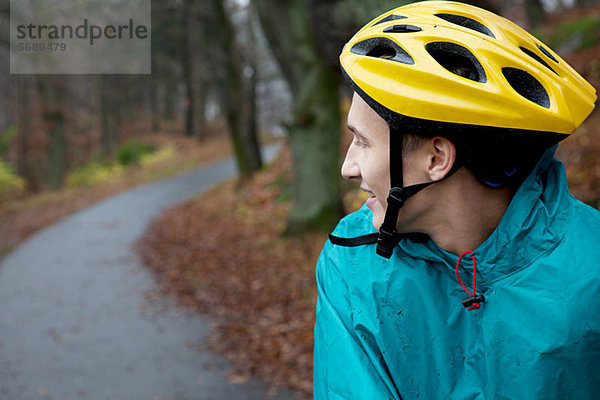 Junger Mann mit Fahrradhelm auf Waldweg und Blick über die Schulter