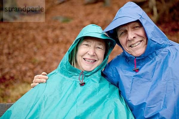 Porträt eines älteren Paares  das auf einer Parkbank sitzt und Wasserdichtheit trägt.